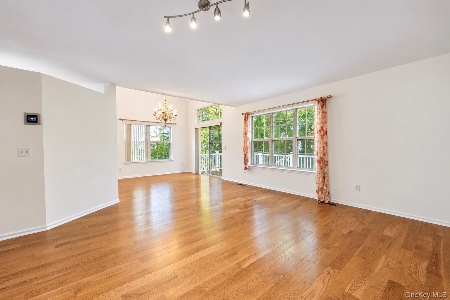 Open-concept interior featuring wood-finish flooring, multi-pane windows, vaulted ceilings, a multi-light track fixture, and a decorative chandelier