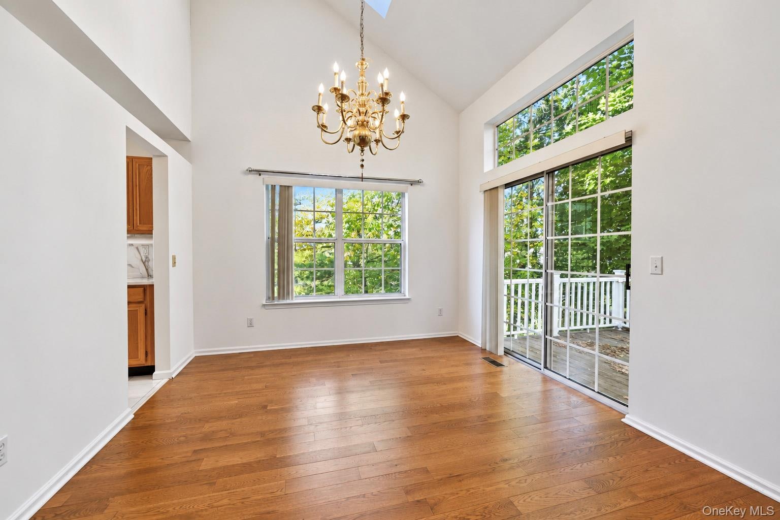 Vaulted ceiling featuring a classic tiered chandelier, wood-finish flooring, and expansive glass sliding doors with overhead transom windows