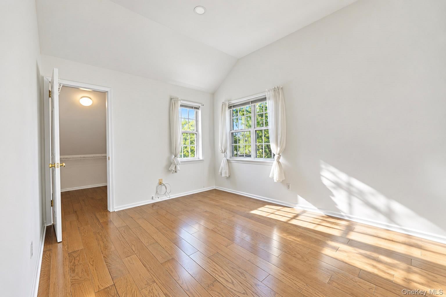 Vaulted ceiling room featuring wood-finish flooring, recessed lighting, and multi-pane windows