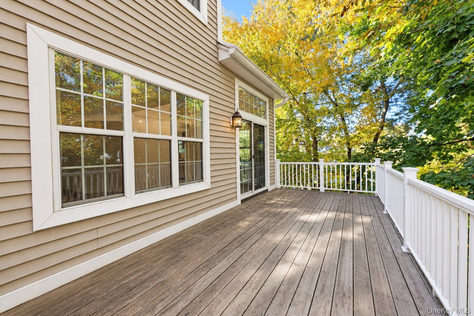 Exterior deck featuring wood-finish plank flooring, white balustrade railings, neutral horizontal siding, and glass sliding doors with multi-light win