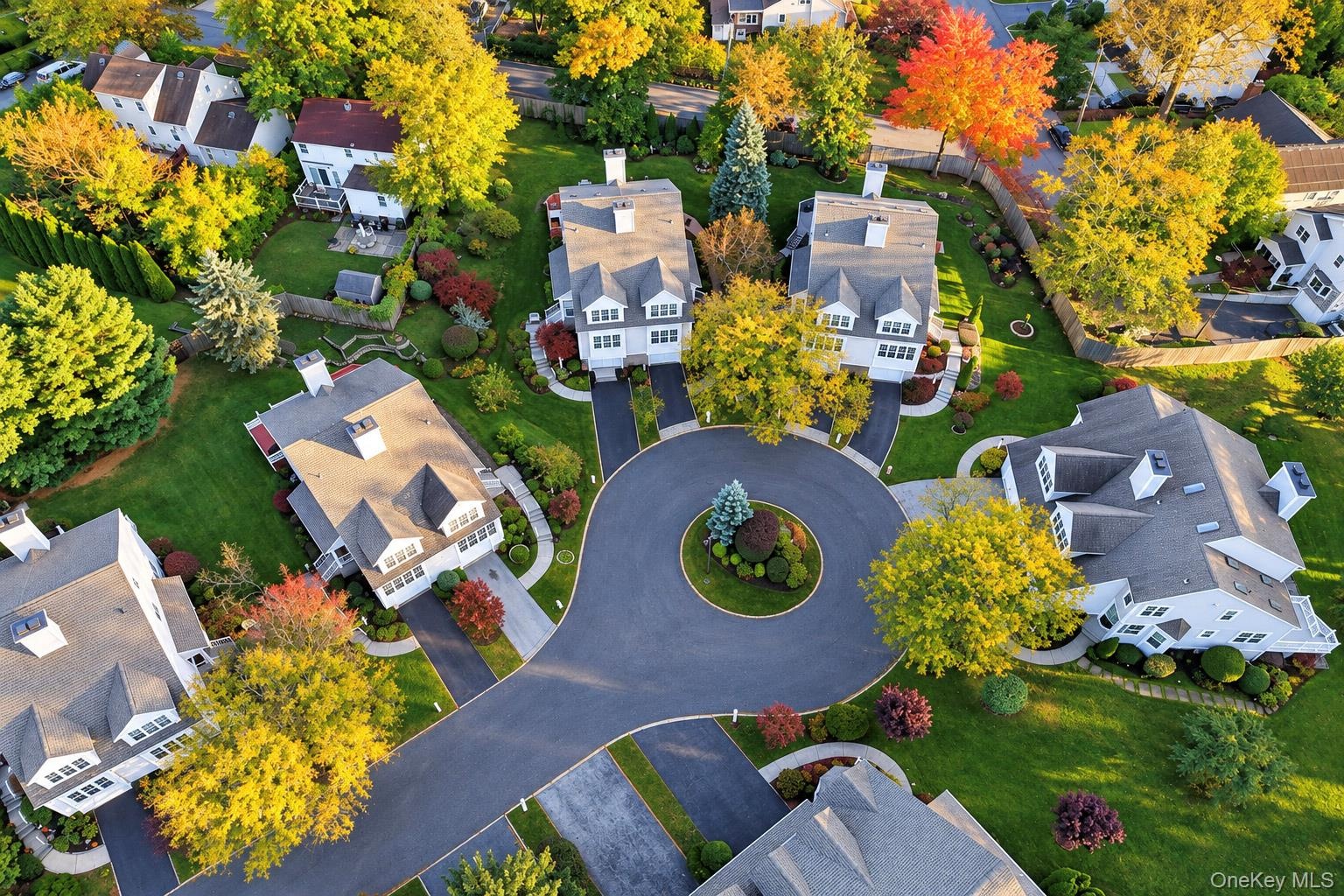 Aerial perspective of a suburban neighborhood featuring multi-story residences, asphalt cul-de-sac, expansive manicured lawns, and mature deciduous tr