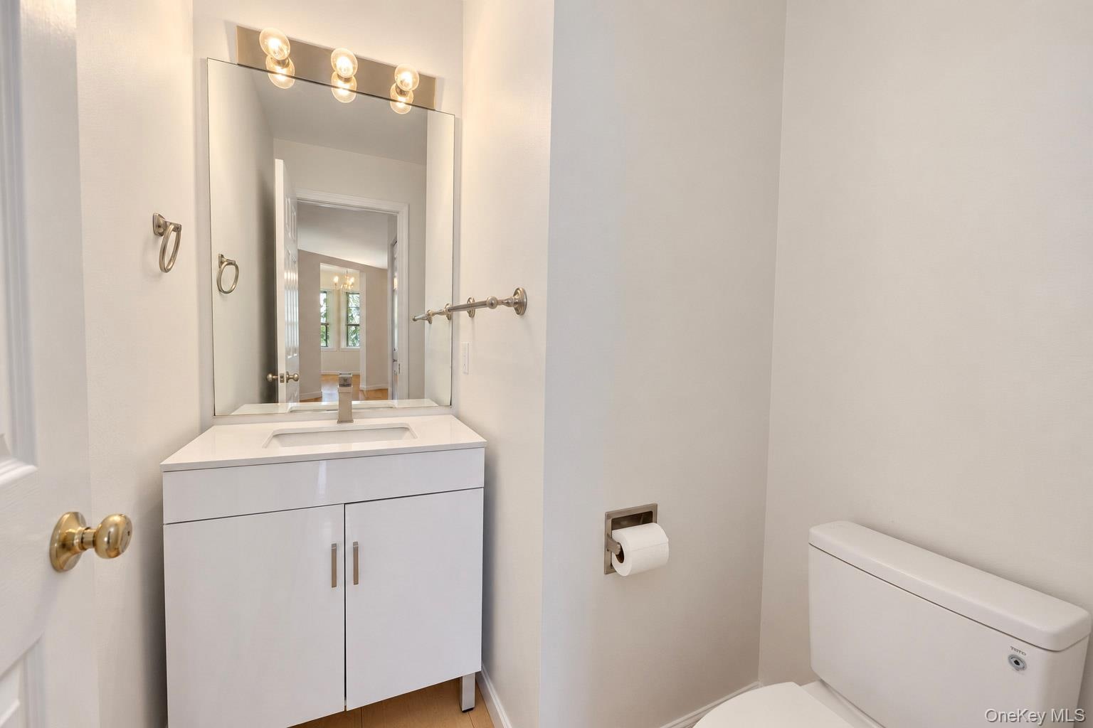 White vanity featuring a solid surface countertop with an integrated rectangular sink, wall-mounted mirror, polished metal multi-bulb light fixture, a
