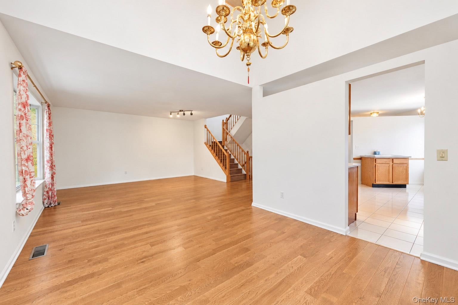 Interior featuring wood-finish flooring, vaulted ceilings, a prominent brass multi-arm chandelier, and a wood-railing staircase
