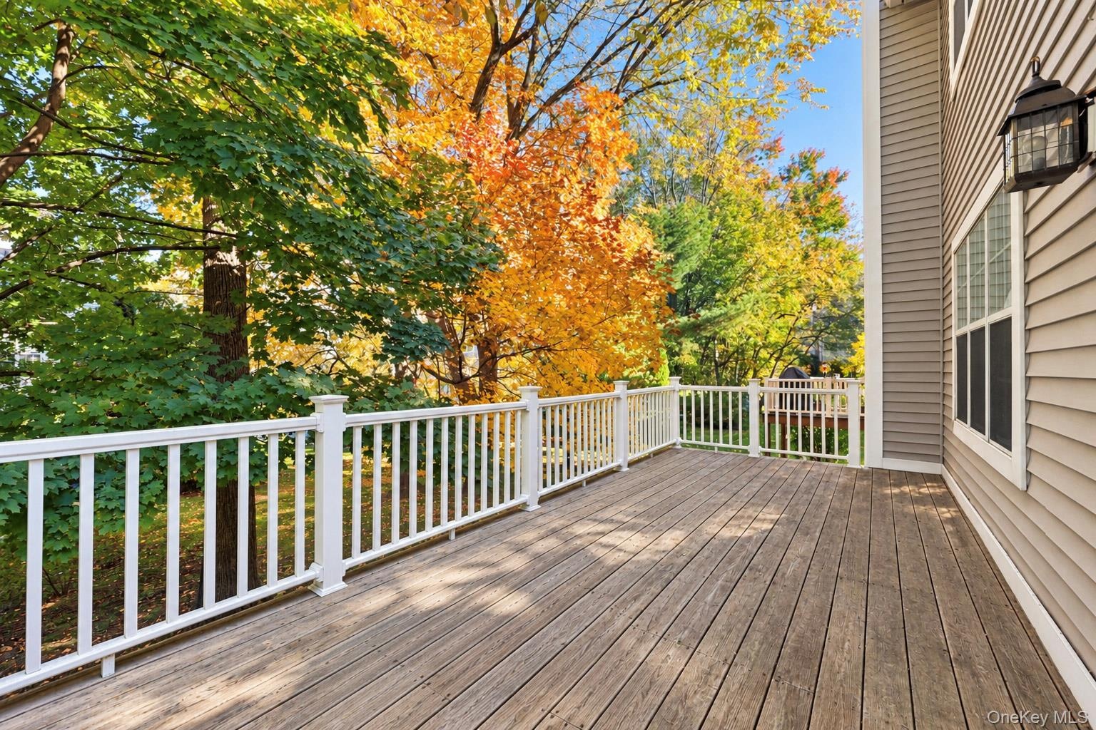 Spacious elevated deck featuring composite plank flooring, white balustrade railings, and wall-mounted exterior lighting