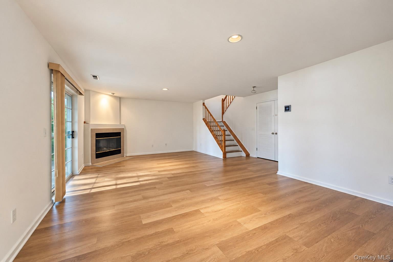 Open-concept interior featuring wood-finish flooring, a corner fireplace with a stone-tile surround, recessed lighting, and a wooden staircase with a 