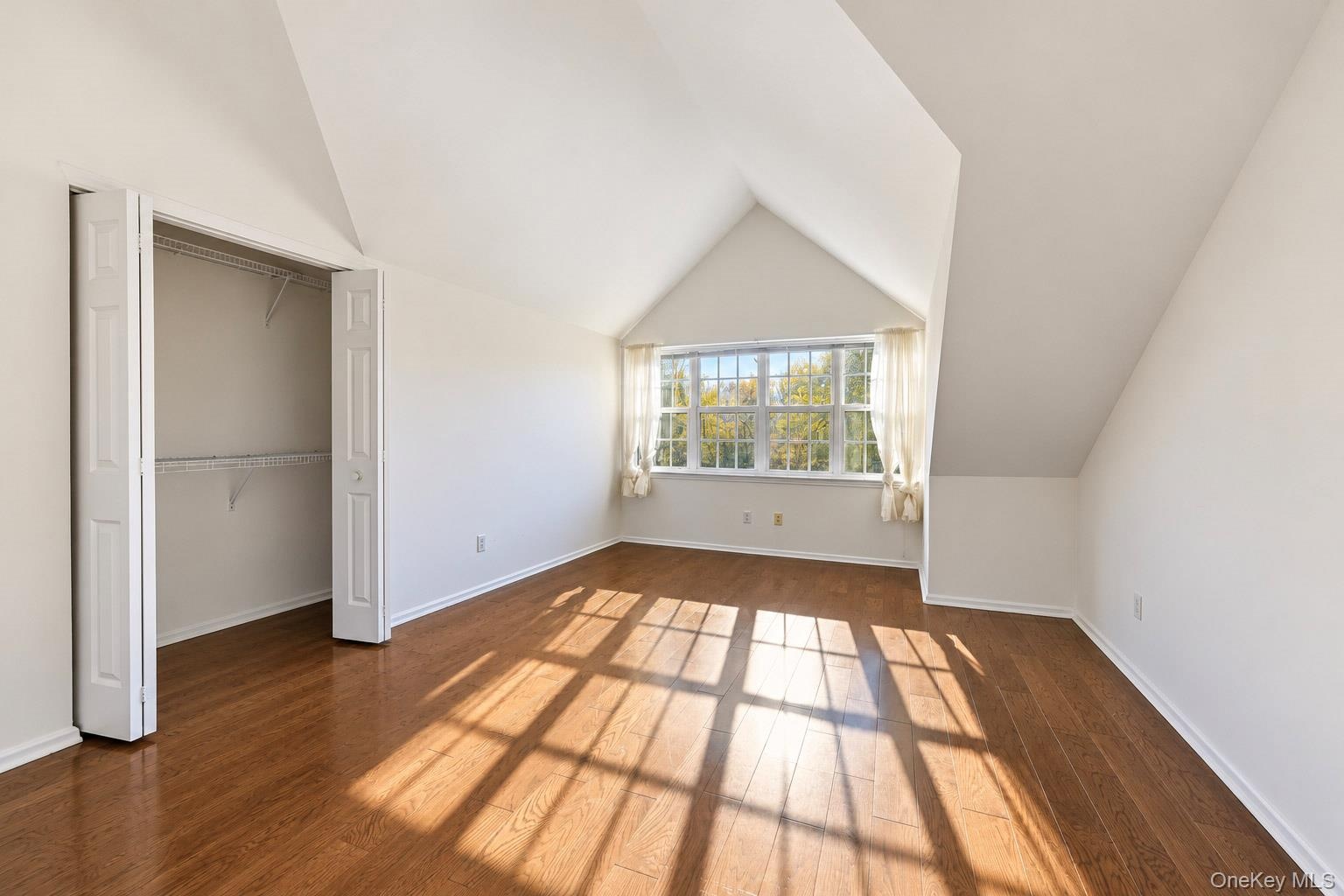 Vaulted ceilings with architectural lines, wood-finish flooring, and a walk-in closet featuring wire shelving