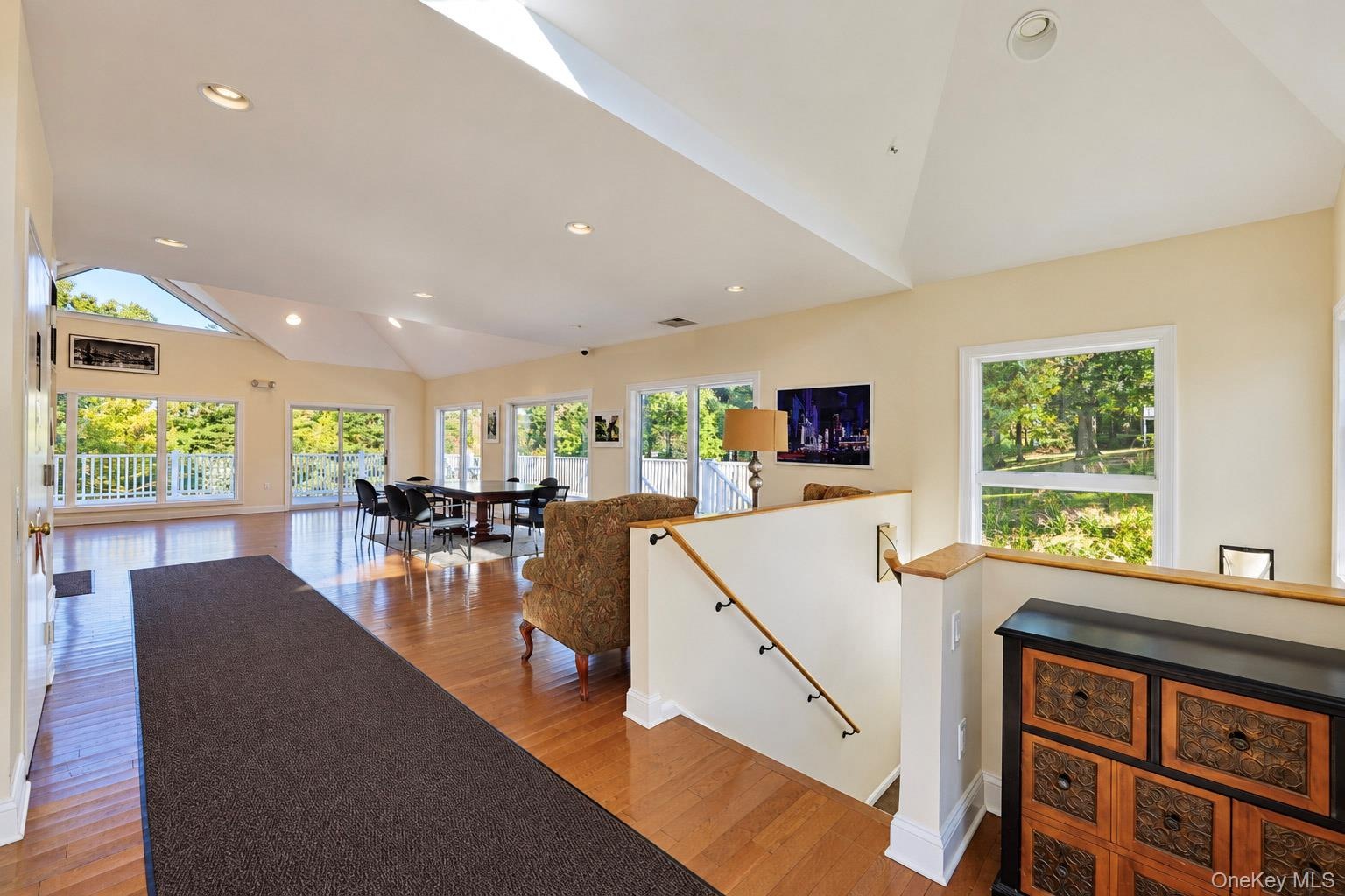 Open-concept living space featuring vaulted ceilings, recessed lighting, wood-finish flooring, and multiple sliding glass doors