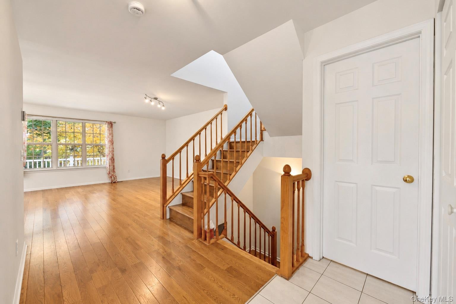 Interior space featuring wood-finish flooring, a staircase with a wooden balustrade, multi-pane window, and tile flooring at the entry