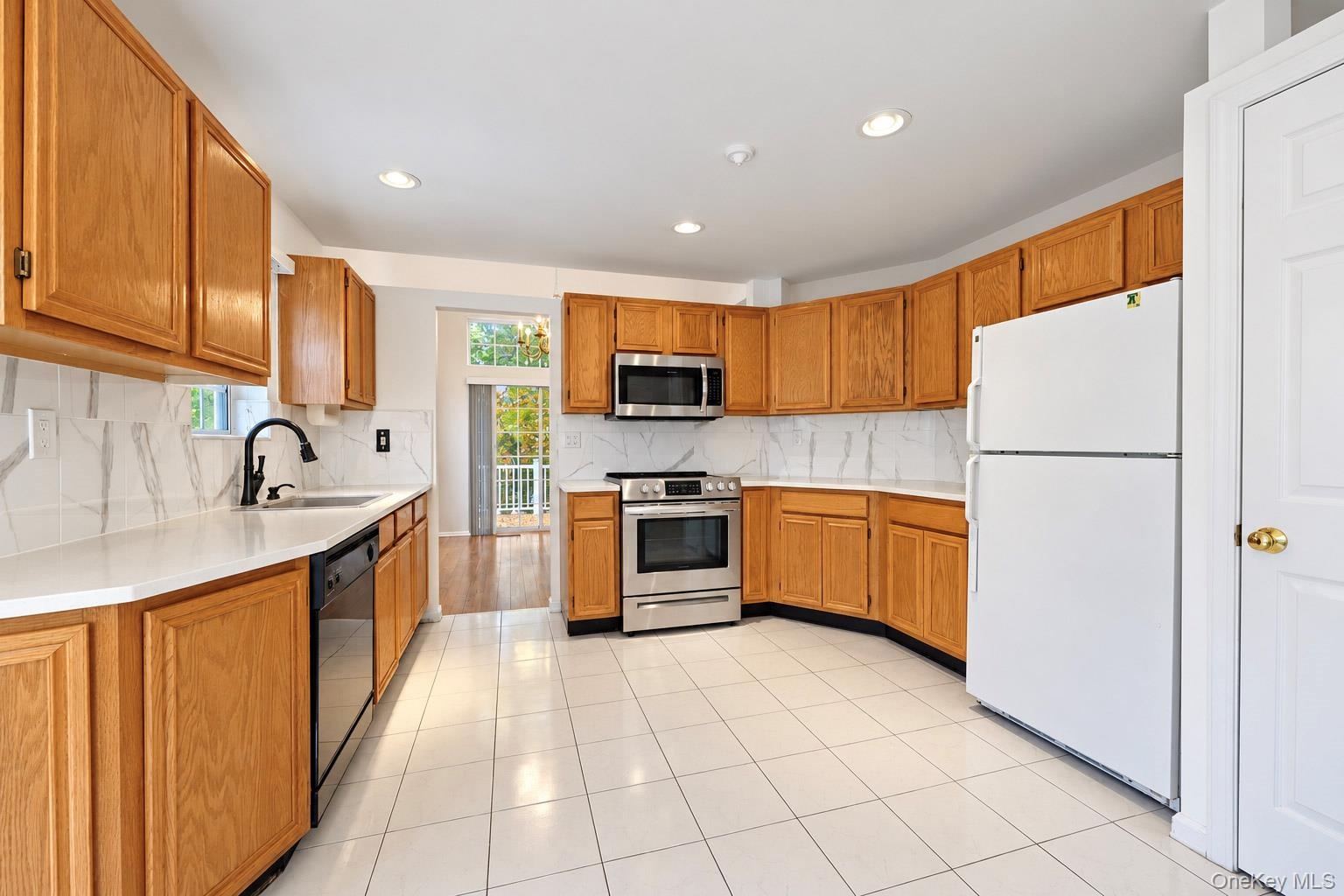 Kitchen featuring wood cabinetry, stone-finish countertops, full-height tile backsplash, stainless steel appliances, and tile flooring