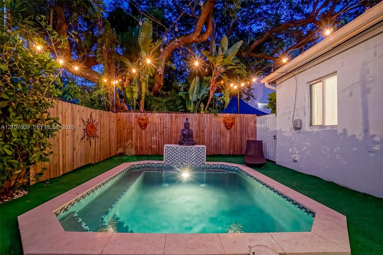 Private rear grounds featuring a custom swimming pool with patterned tile water feature, perimeter wood privacy fencing, and mature tropical landscapi