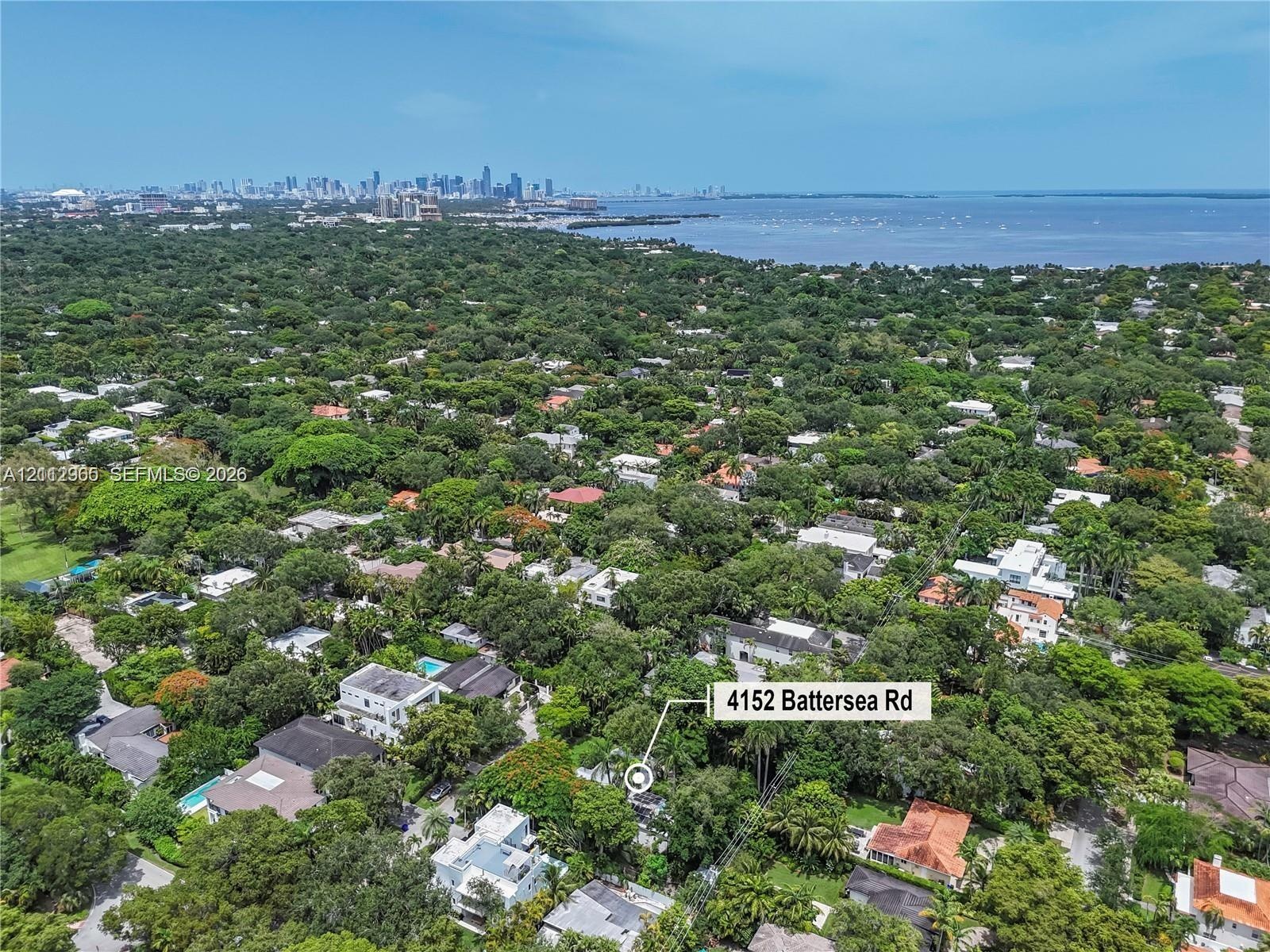 Aerial perspective of 4152 Battersea Rd, featuring dense mature tree canopy, proximity to the coastline, and urban skyline backdrop