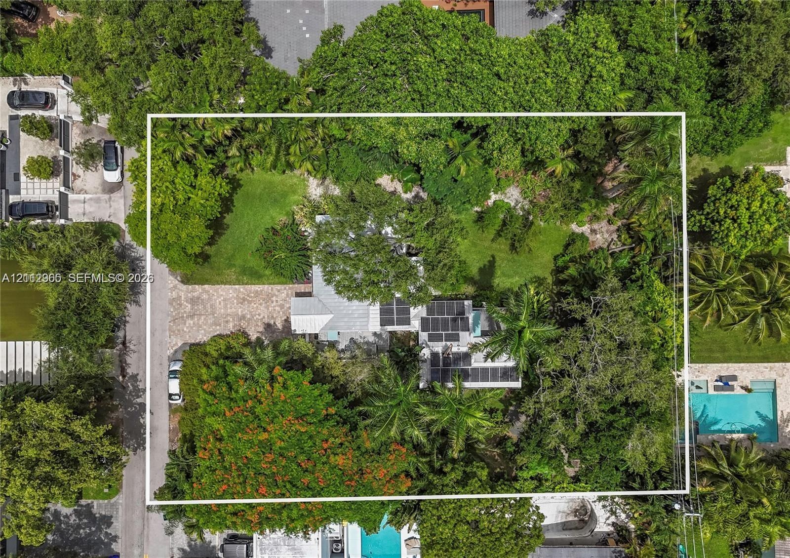 Aerial view featuring a paved driveway, solar panel installation, mature tree canopy, and landscaped grounds