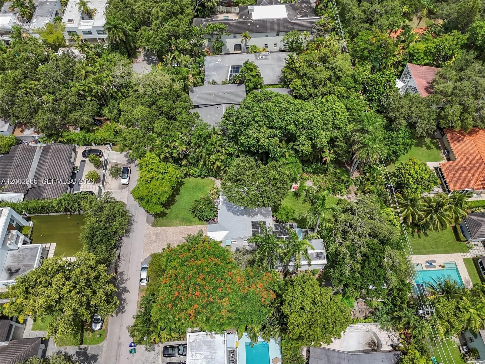 Aerial perspective of a property featuring mature tree canopy, expansive lawn space, and hardscaped driveway area