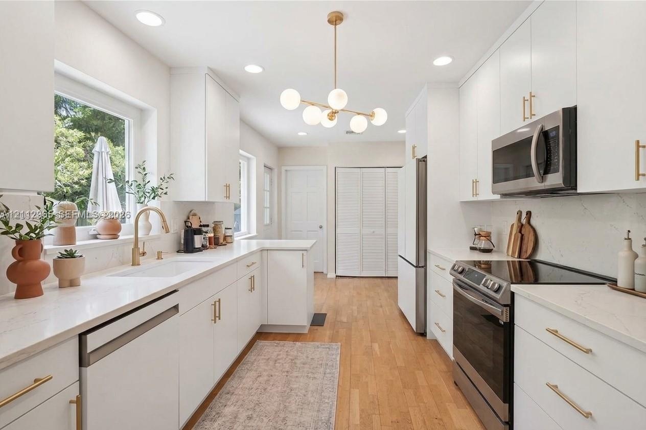 Kitchen featuring white cabinetry with gold-toned hardware, solid-surface countertops, wood-finish flooring, stainless steel appliances, and a modern 