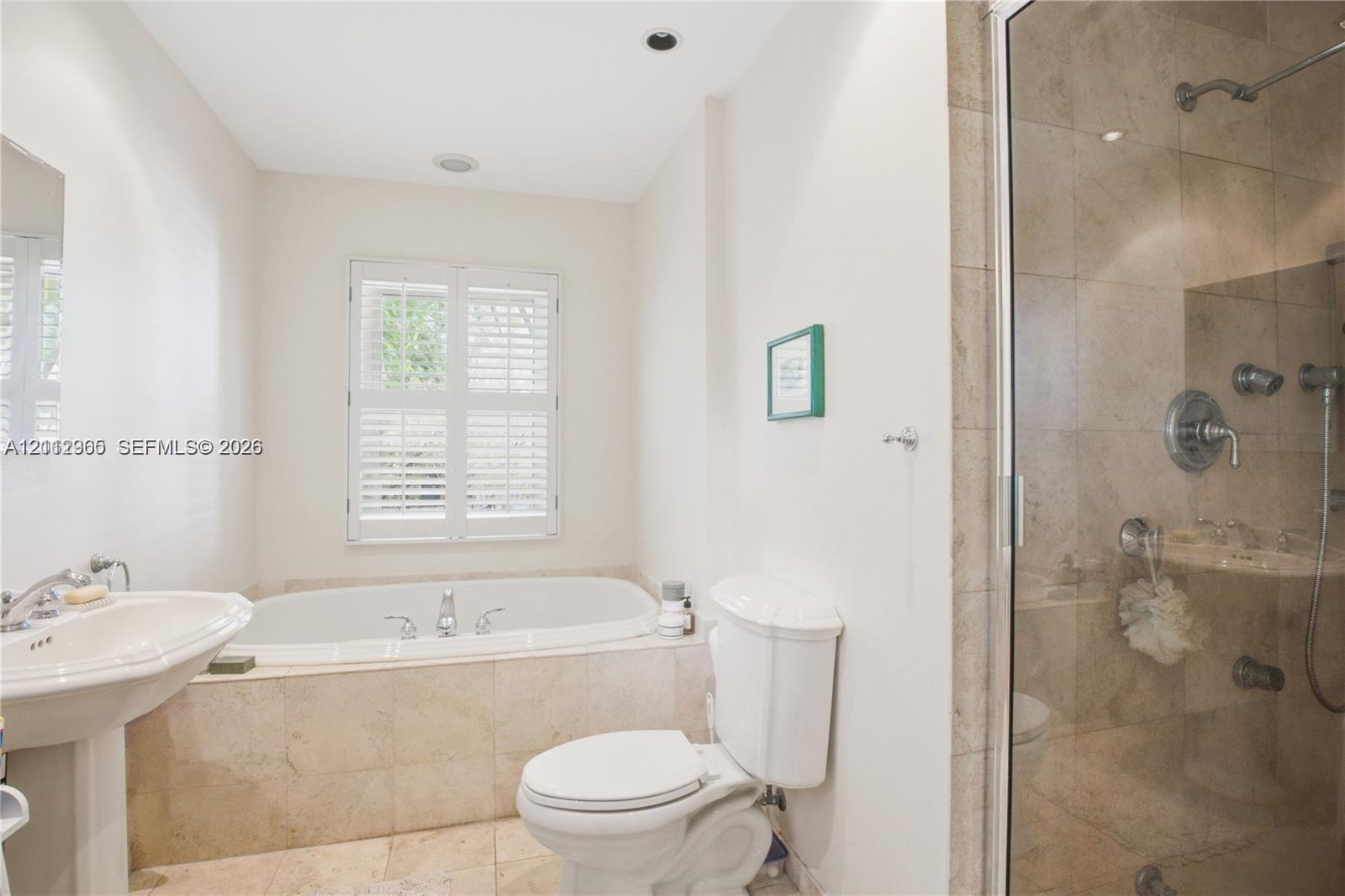 Bathroom featuring a pedestal sink, soaking tub with tile surround, glass-enclosed shower with metallic fixtures, and plantation shutters