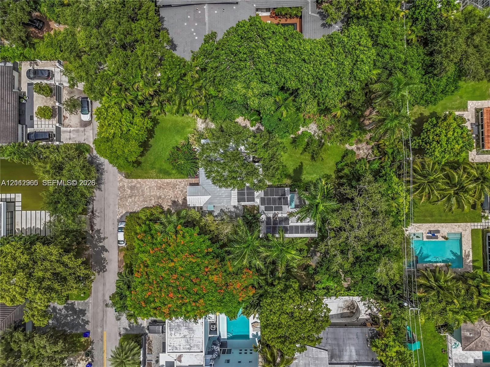 Aerial perspective featuring mature tree canopy, paver driveway, and roof-mounted solar panels