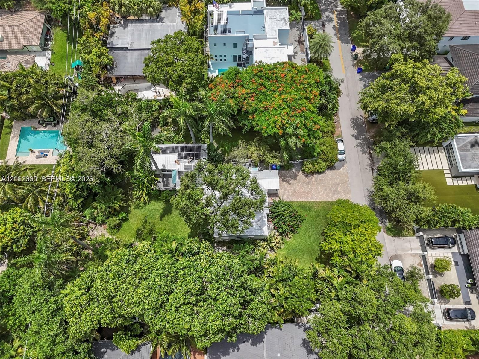 Aerial perspective of a property featuring solar panels, a paved driveway, and mature landscaping with expansive tree canopy