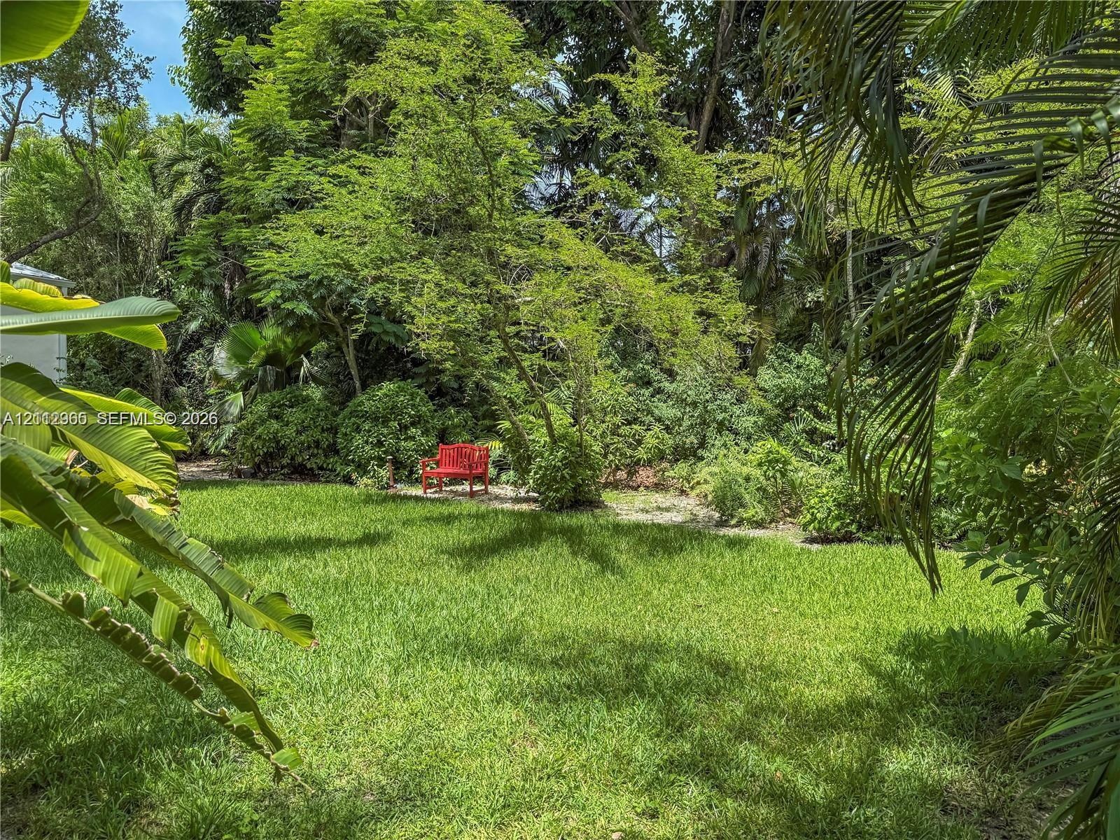 Expansive backyard featuring a lush lawn, mature trees, dense greenery, and a gravel garden area