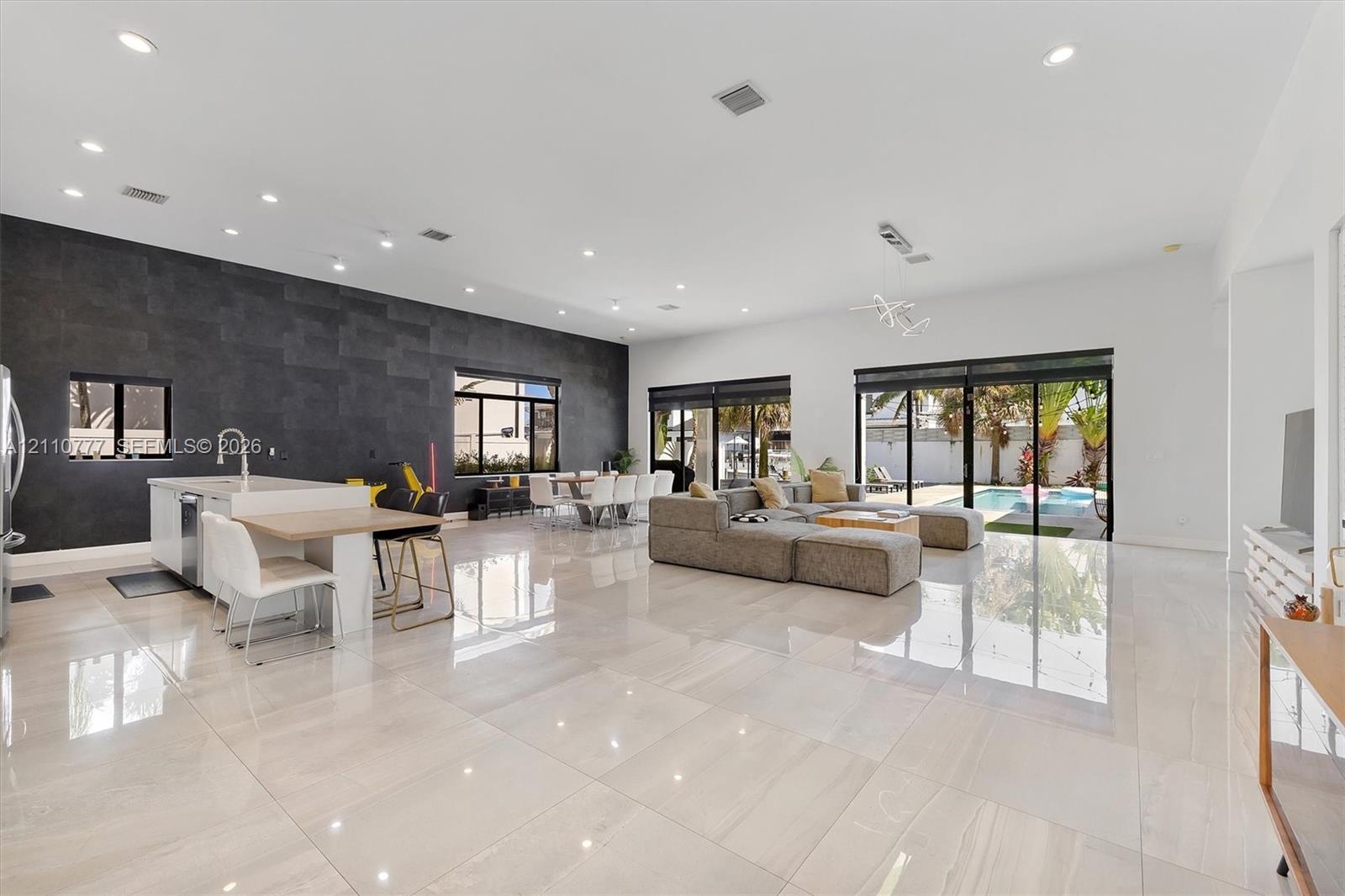 Open-concept living space featuring high-gloss tile flooring, recessed lighting, a statement dark tile accent wall, an island kitchen with built-in ca