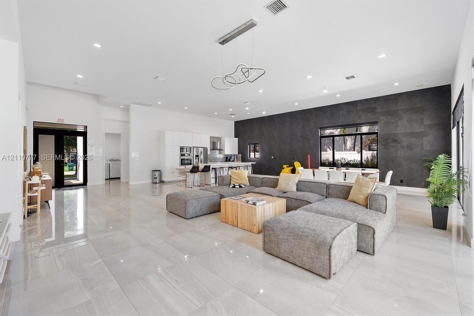 Open-concept living space featuring high ceilings with recessed lighting, large-format tile flooring, a charcoal stone-finish accent wall, and contemp