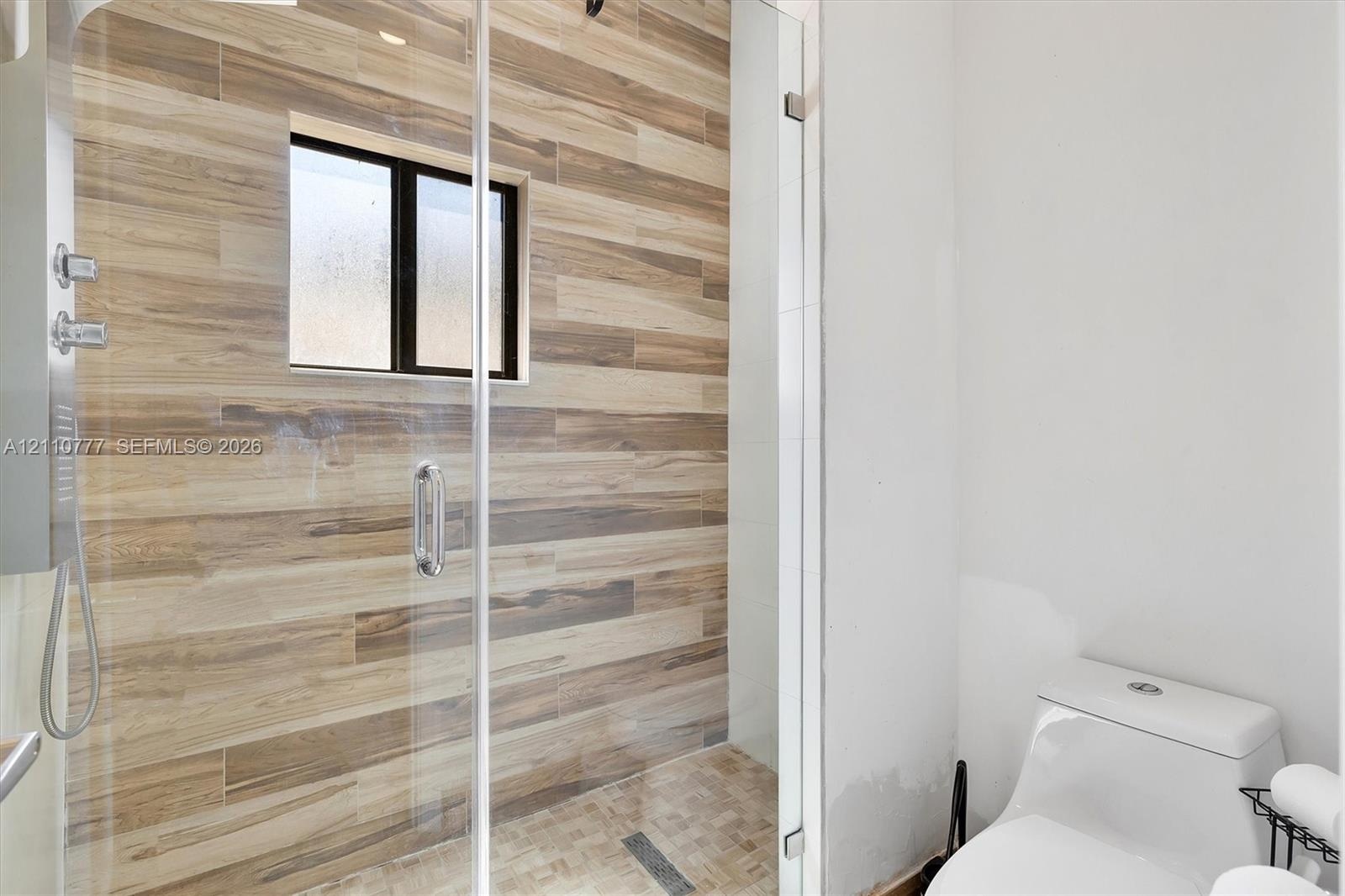 Walk-in shower featuring wood-finish tile wall cladding, frameless glass enclosure, wall-mounted shower fixture, and a built-in window, paired with a 