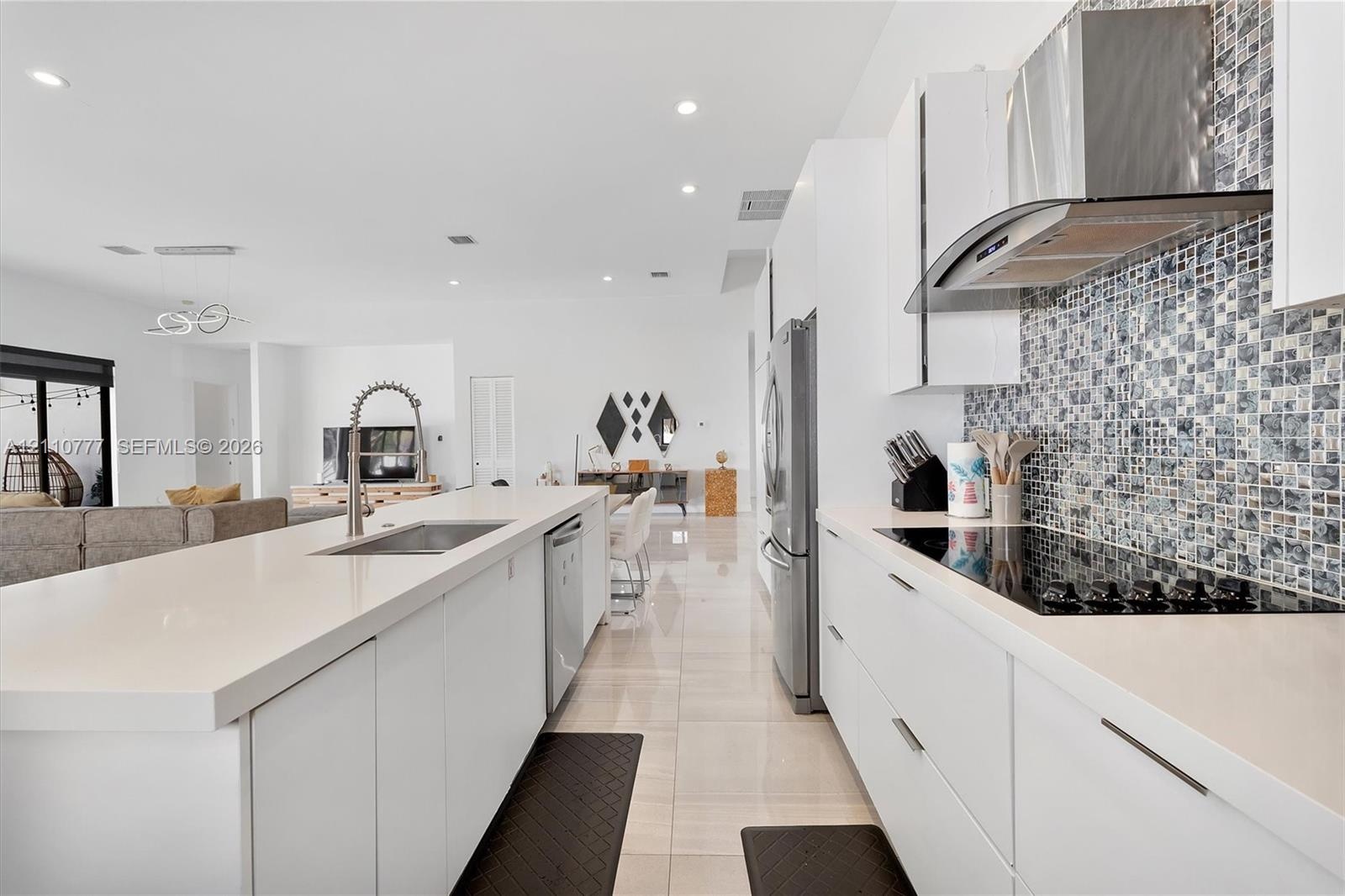 Kitchen featuring flat-panel white cabinetry, quartz countertops, a mosaic tile backsplash, a stainless steel range hood, and large-format tile floori