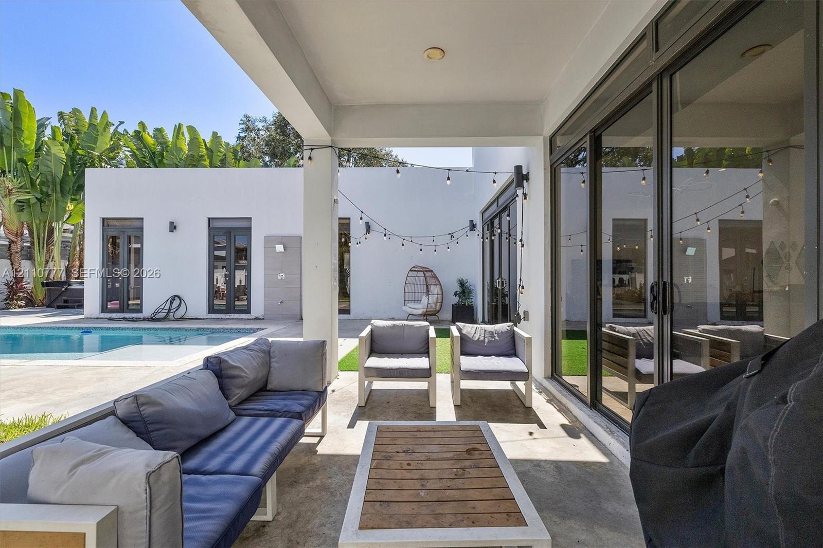Covered patio featuring concrete flooring, sliding glass door systems, recessed ceiling lighting, and overhead string lights, situated near a swimming