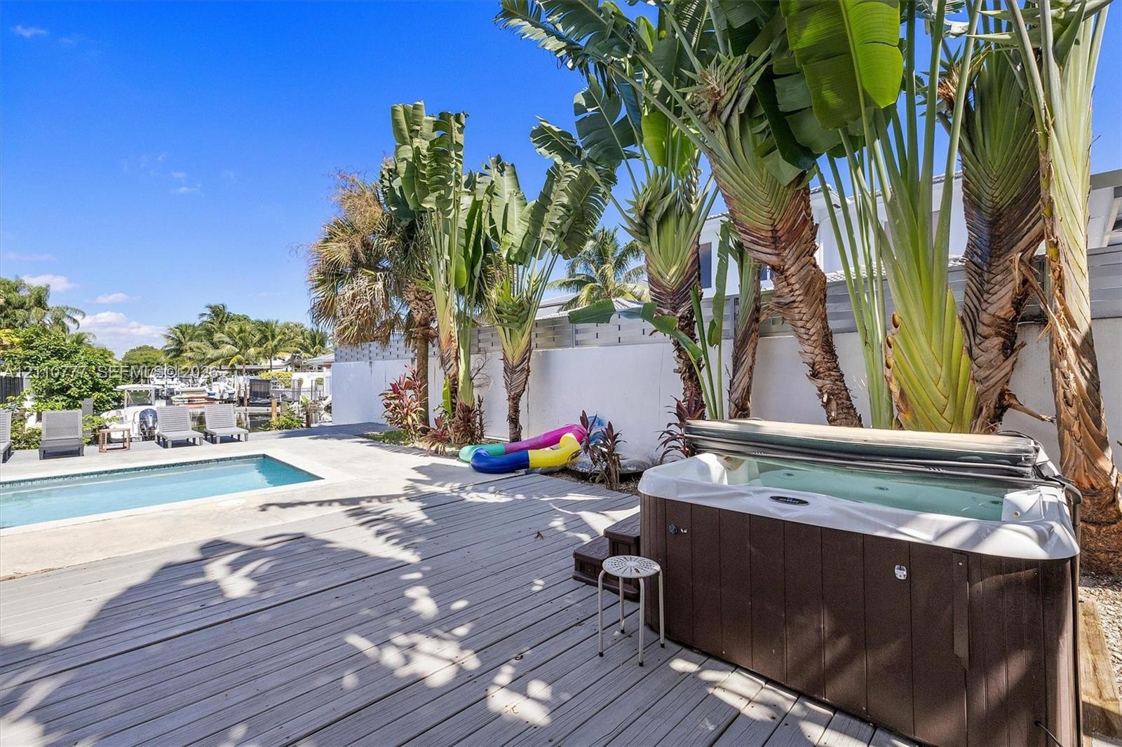 Outdoor area featuring a swimming pool, wood-finish decking, an integrated spa, and mature tropical landscaping