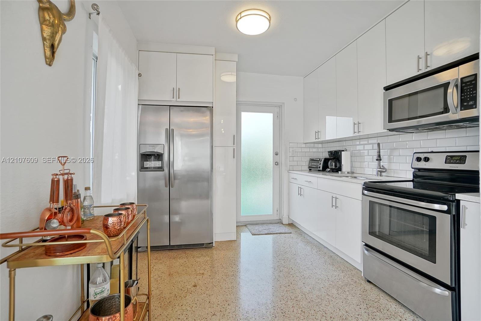 Kitchen featuring white high-gloss cabinetry, stainless steel appliances, subway tile backsplash, and terrazzo flooring