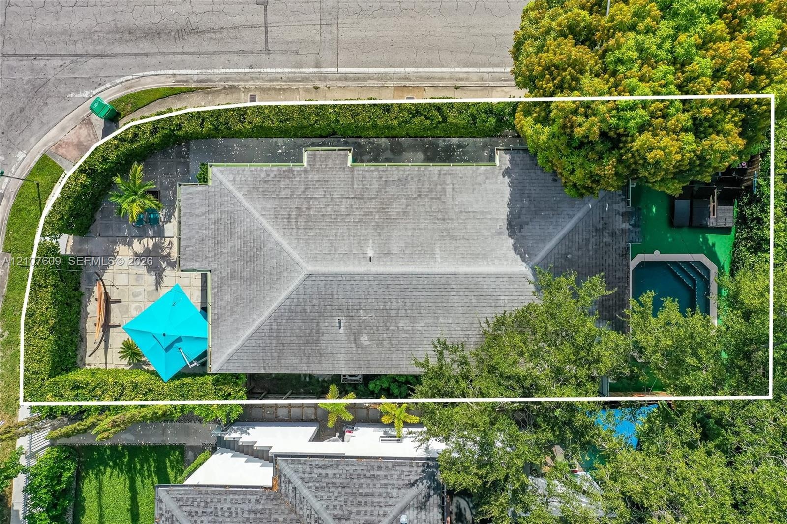 Aerial perspective featuring a shingle roof, a rectangular inground pool, expansive stone-paver hardscaping, mature perimeter hedges, and established 
