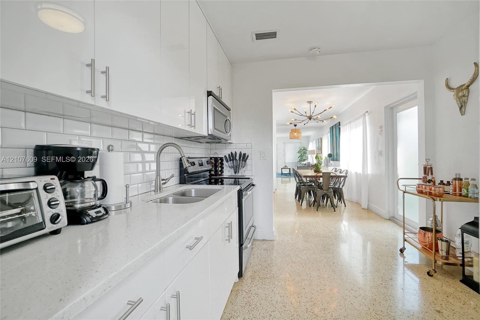 Kitchen featuring white flat-panel cabinetry, light-toned stone-surface countertops, a double-basin stainless steel sink with gooseneck faucet, white 