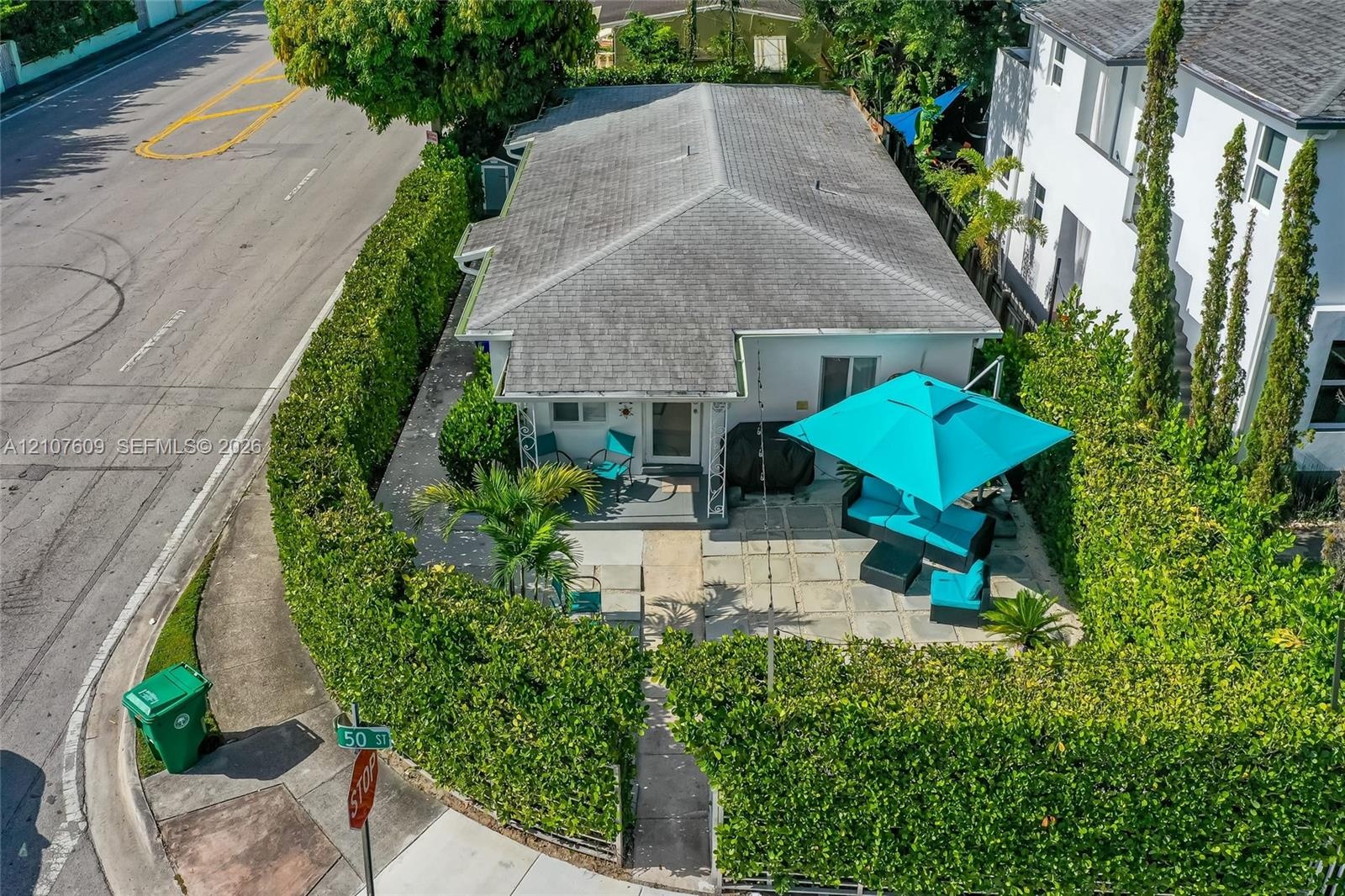 Exterior featuring a hip roof, paved patio, and perimeter hedges providing privacy