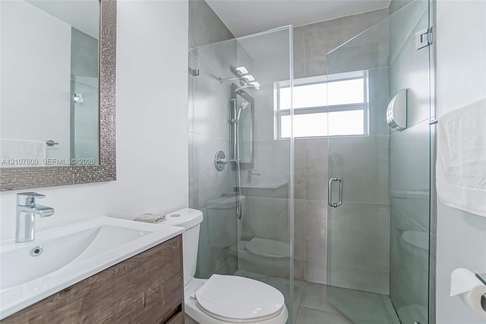 Bathroom featuring a wood-finish floating vanity, integrated sink with chrome faucet, framed mirror, and a walk-in shower enclosed by glass paneling w