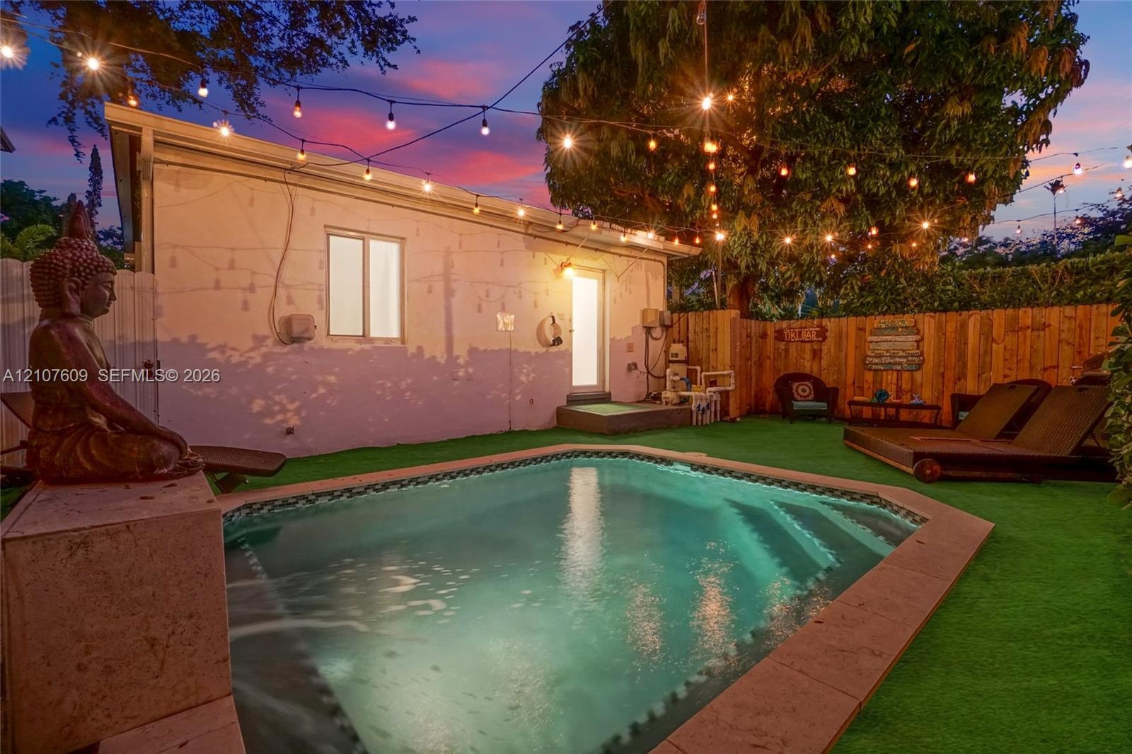 Backyard featuring an in-ground pool with stepped entry, stone-finish coping, synthetic turf ground cover, and perimeter wood privacy fencing