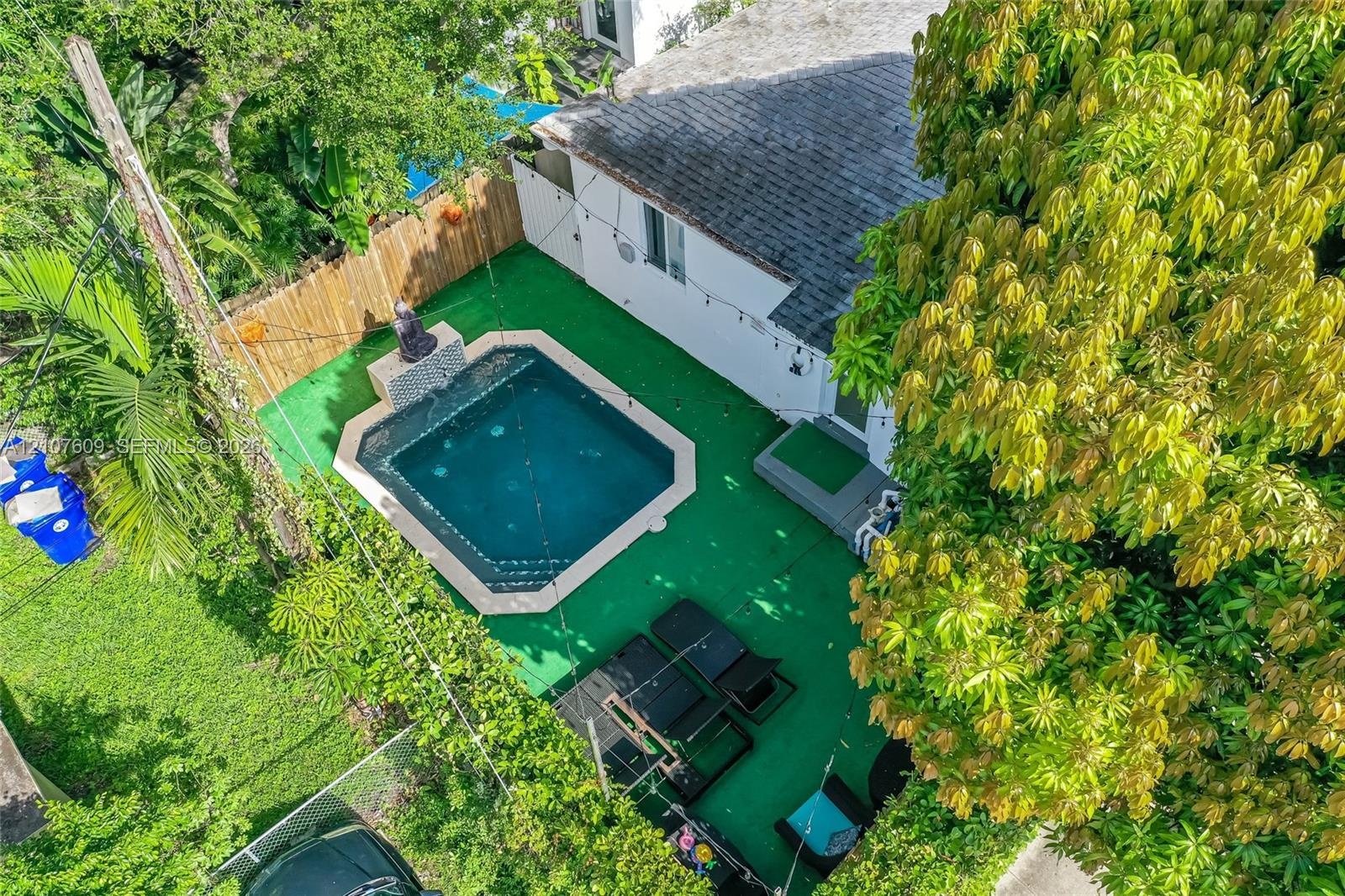 Backyard featuring an in-ground pool with stone coping, synthetic turf surfacing, wood-plank fencing, and mature trees