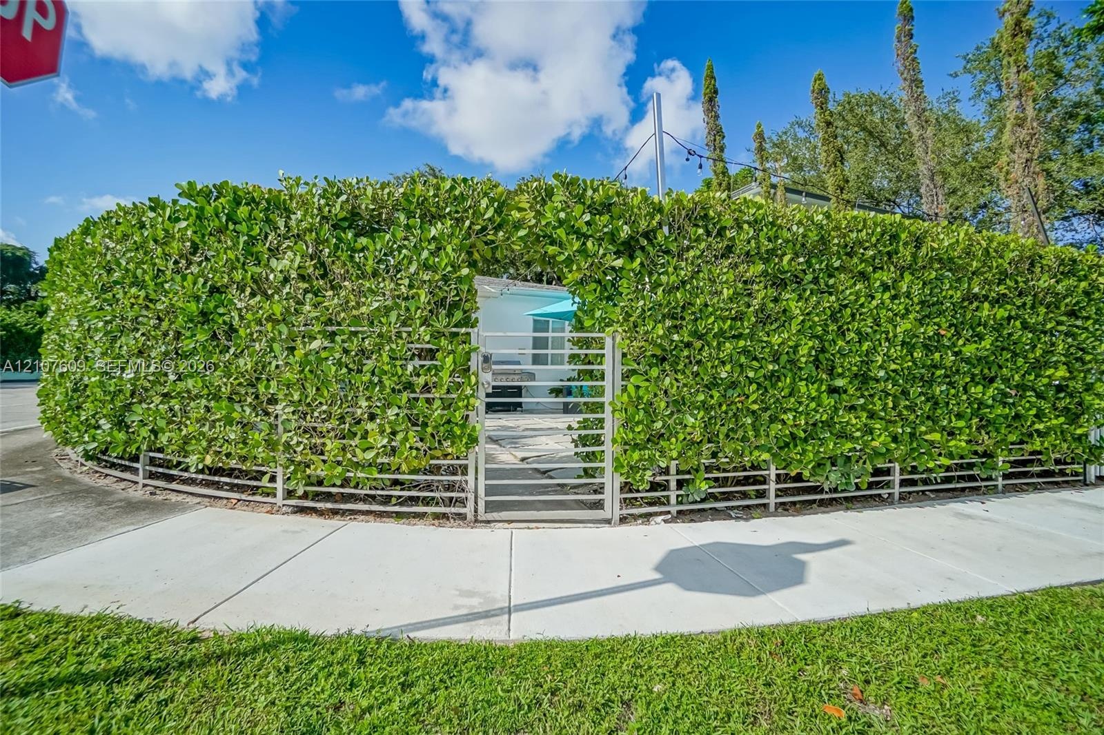 Exterior grounds featuring a tall privacy hedge, gated metal entrance, and paved walkway