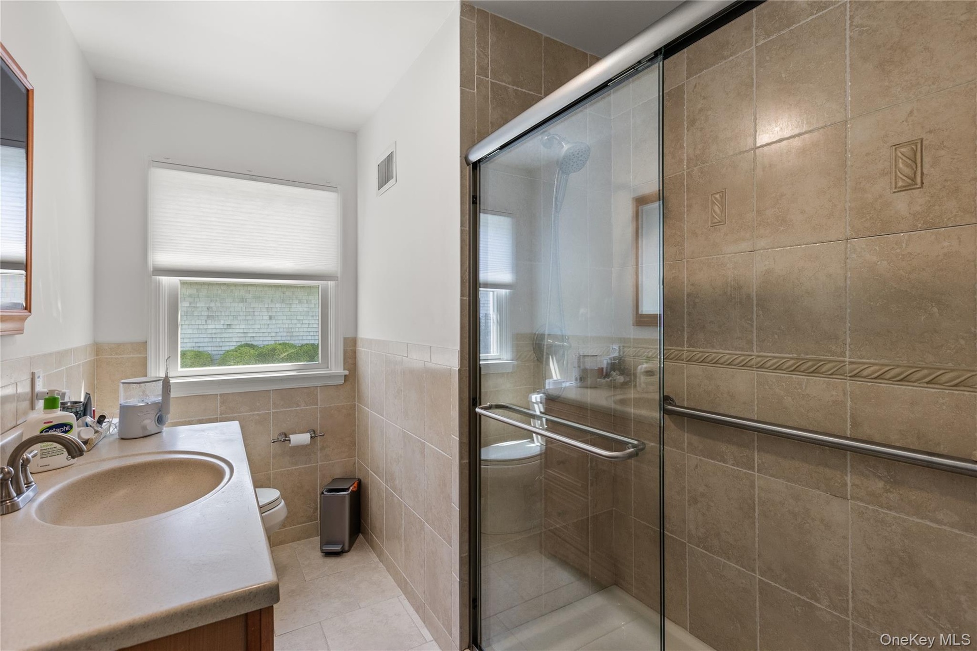 Full bathroom with vanity, a shower stall, tile walls, light tile patterned floors, and a wainscoted wall