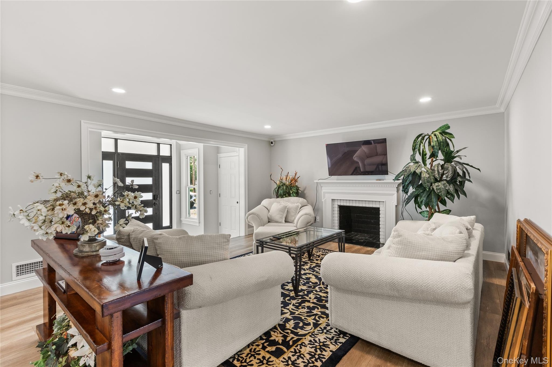 Living area featuring light wood-style flooring, a brick fireplace, crown molding, and recessed lighting