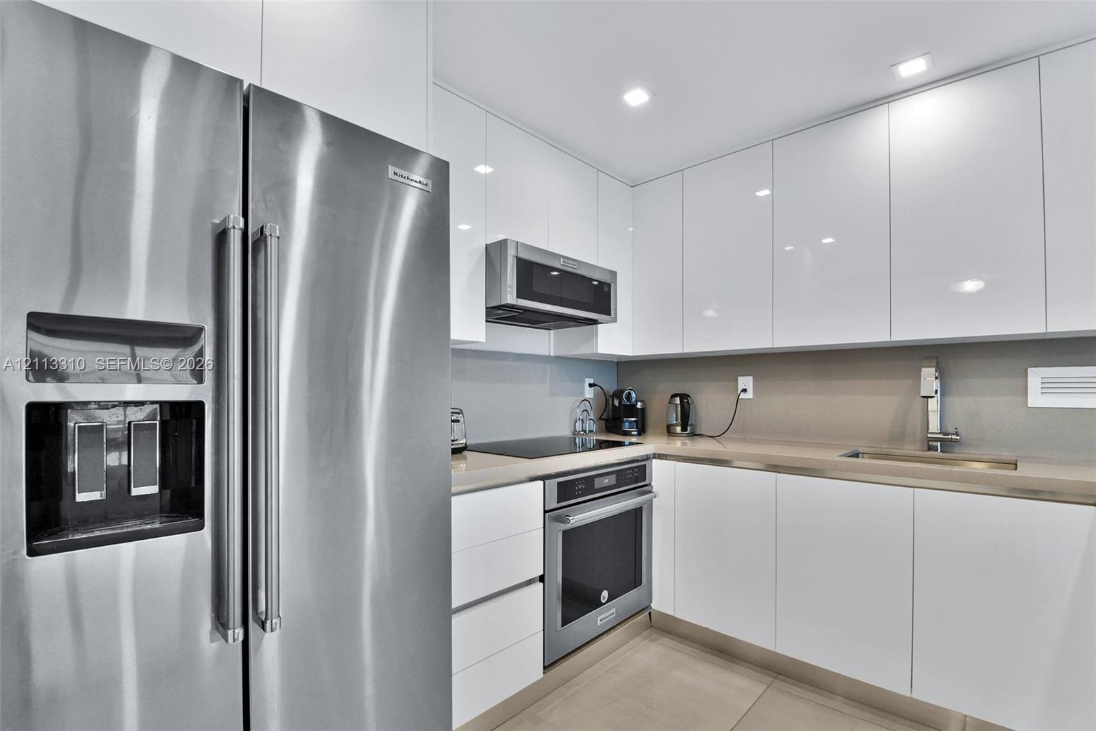 Kitchen featuring high-gloss white cabinetry, solid surface countertops, recessed lighting, and stainless steel appliances including a built-in oven, 
