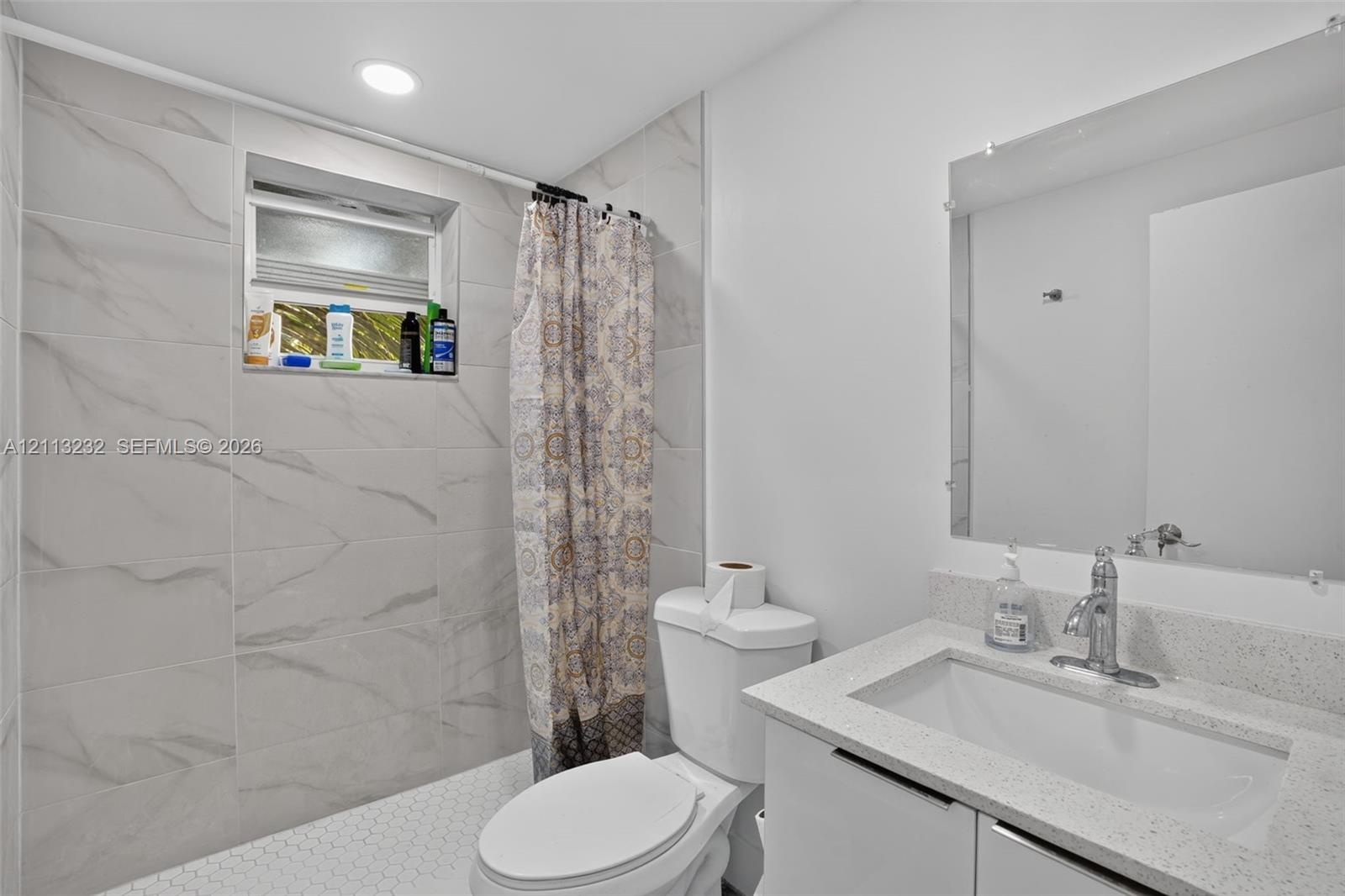 Bathroom featuring large-format stone-finish wall tiling, white vanity with a speckled countertop, integrated sink, chrome faucet, and a frameless mir