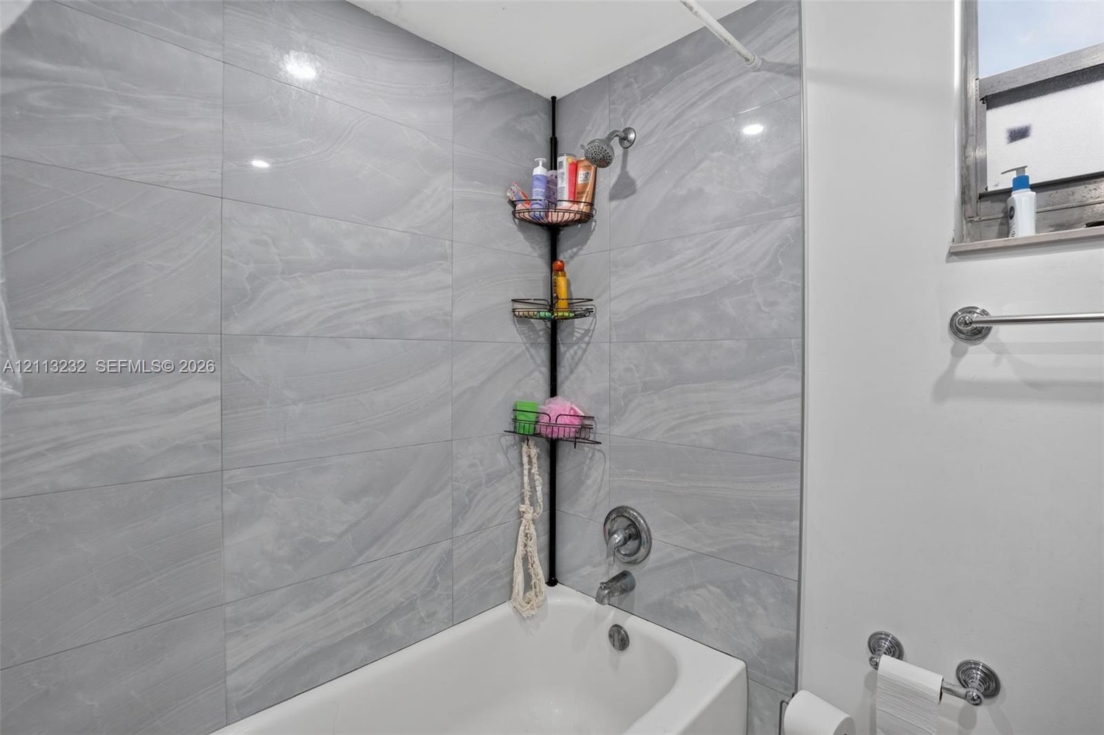 Bathtub surround featuring large-format gray veined tile, integrated metallic shower head, and wall-mounted metal towel rack