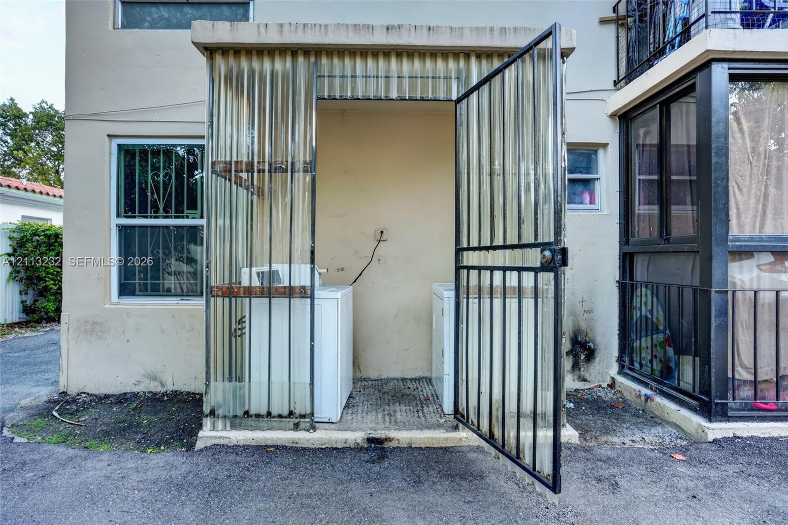 Exterior laundry area enclosed by corrugated polycarbonate panels and a metal security gate