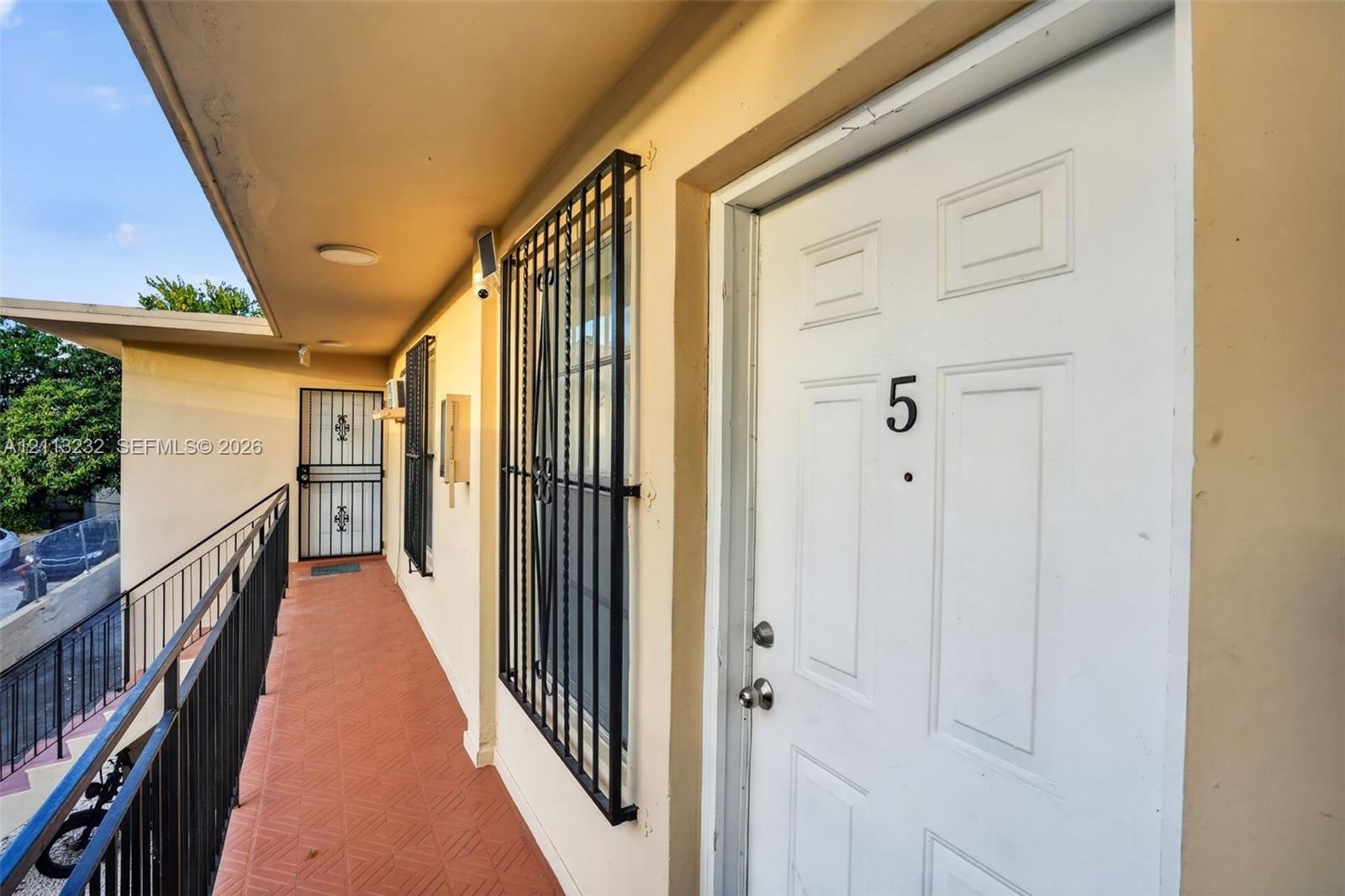 Exterior walkway with tiled flooring, metal railings, and unit entry door featuring protective iron security bars on window openings