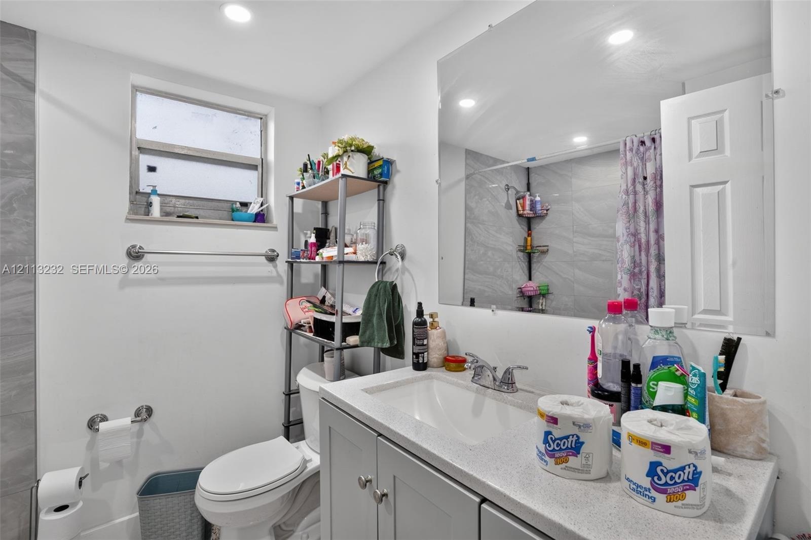 Bathroom featuring gray shaker-style vanity cabinetry, solid-surface countertop with integrated basin, polished chrome faucet, large-format wall tilin