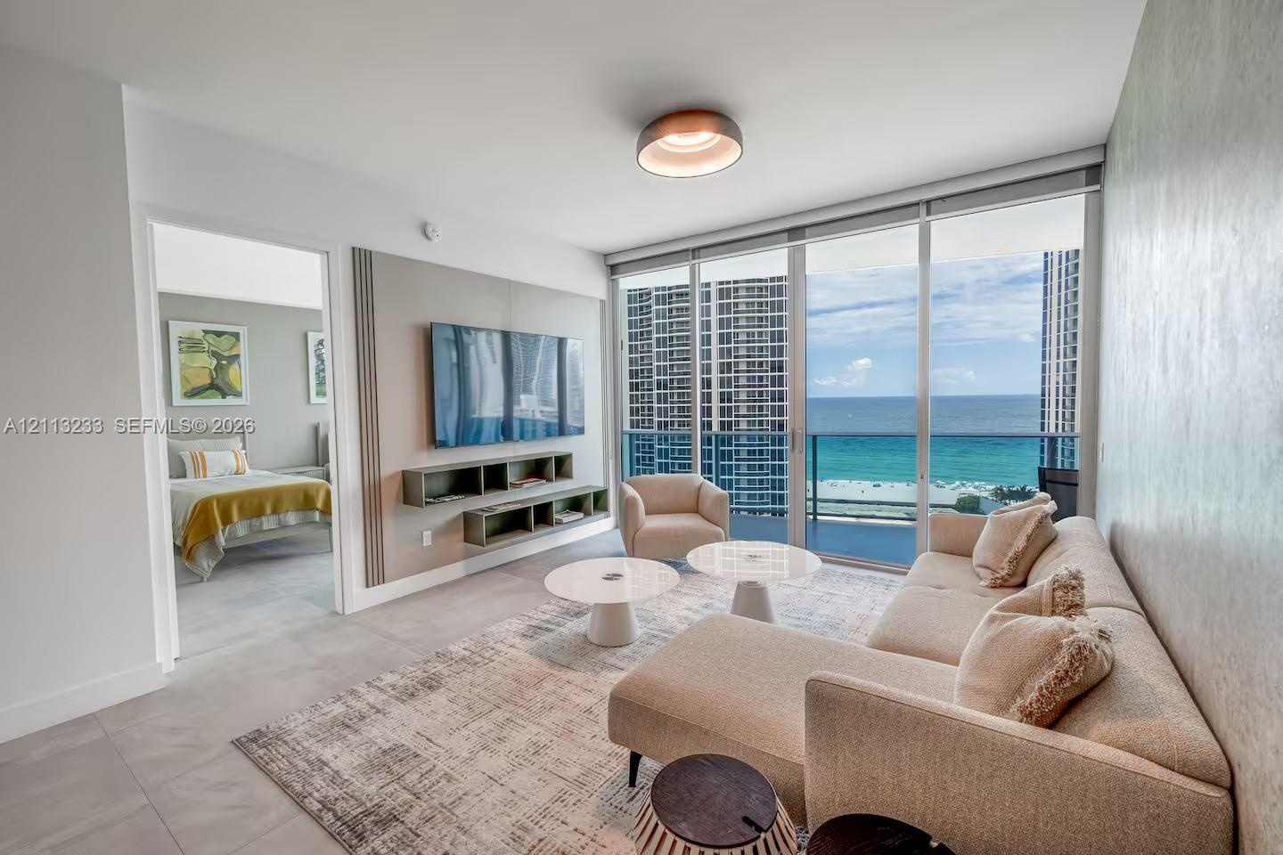 Living space featuring floor-to-ceiling glass sliding doors, custom wall-mounted media shelving, recessed ceiling lighting, and large-format tile floo