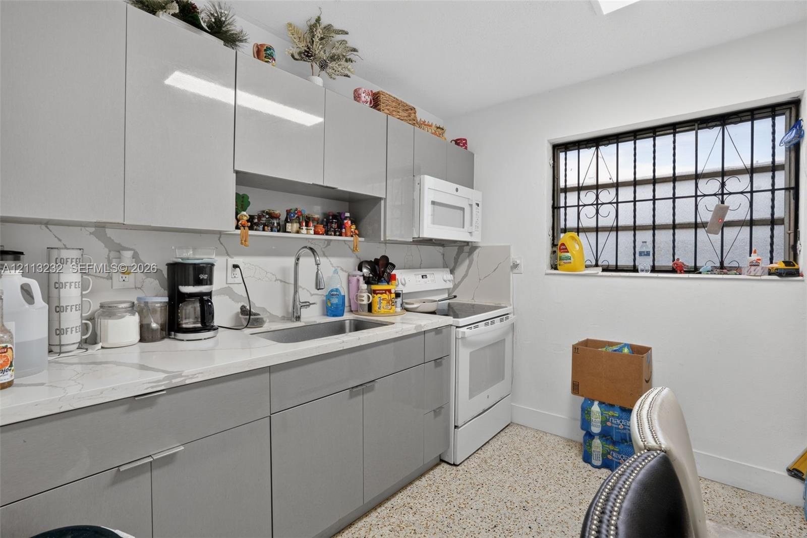 Kitchen featuring high-gloss gray cabinetry, stone-patterned countertops, a full-height stone-patterned backsplash, undermount stainless steel sink wi