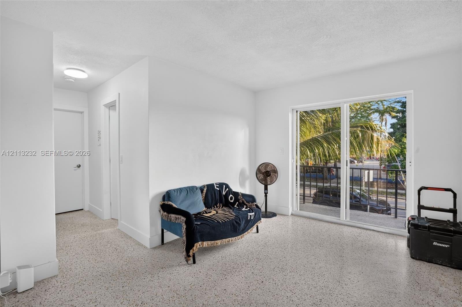 Interior space featuring polished stone-aggregate flooring, white walls, and a large sliding glass door with a metal balcony railing