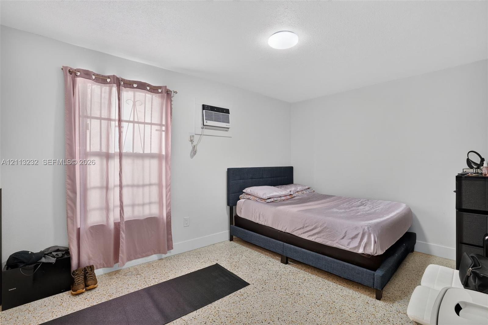 Room featuring light-toned interior walls, neutral speckled flooring, a mounted air conditioning unit, and a flush-mount ceiling light