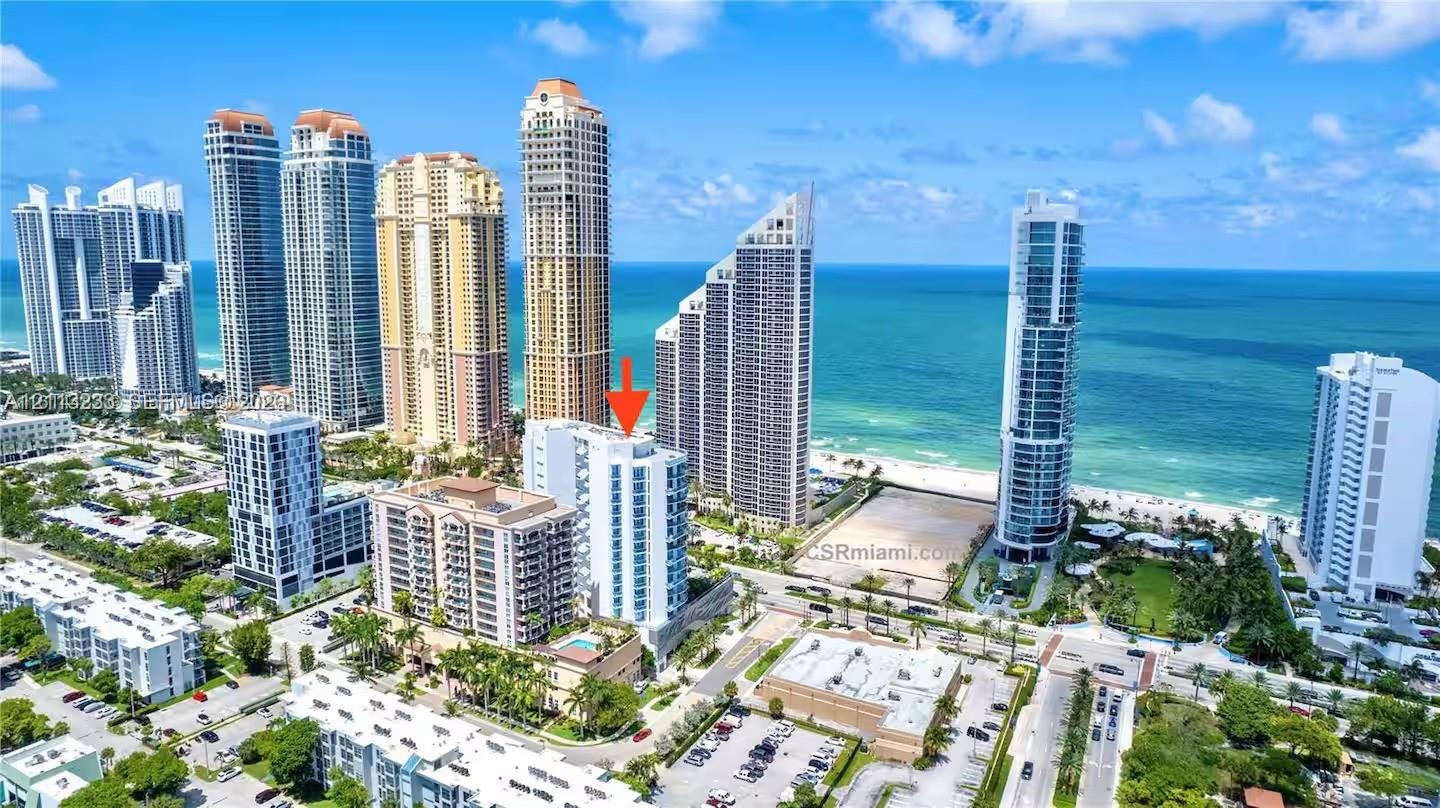 Aerial perspective of a high-rise residential building featuring a glass-facade exterior, multiple balconies, and a ground-level swimming pool, situat