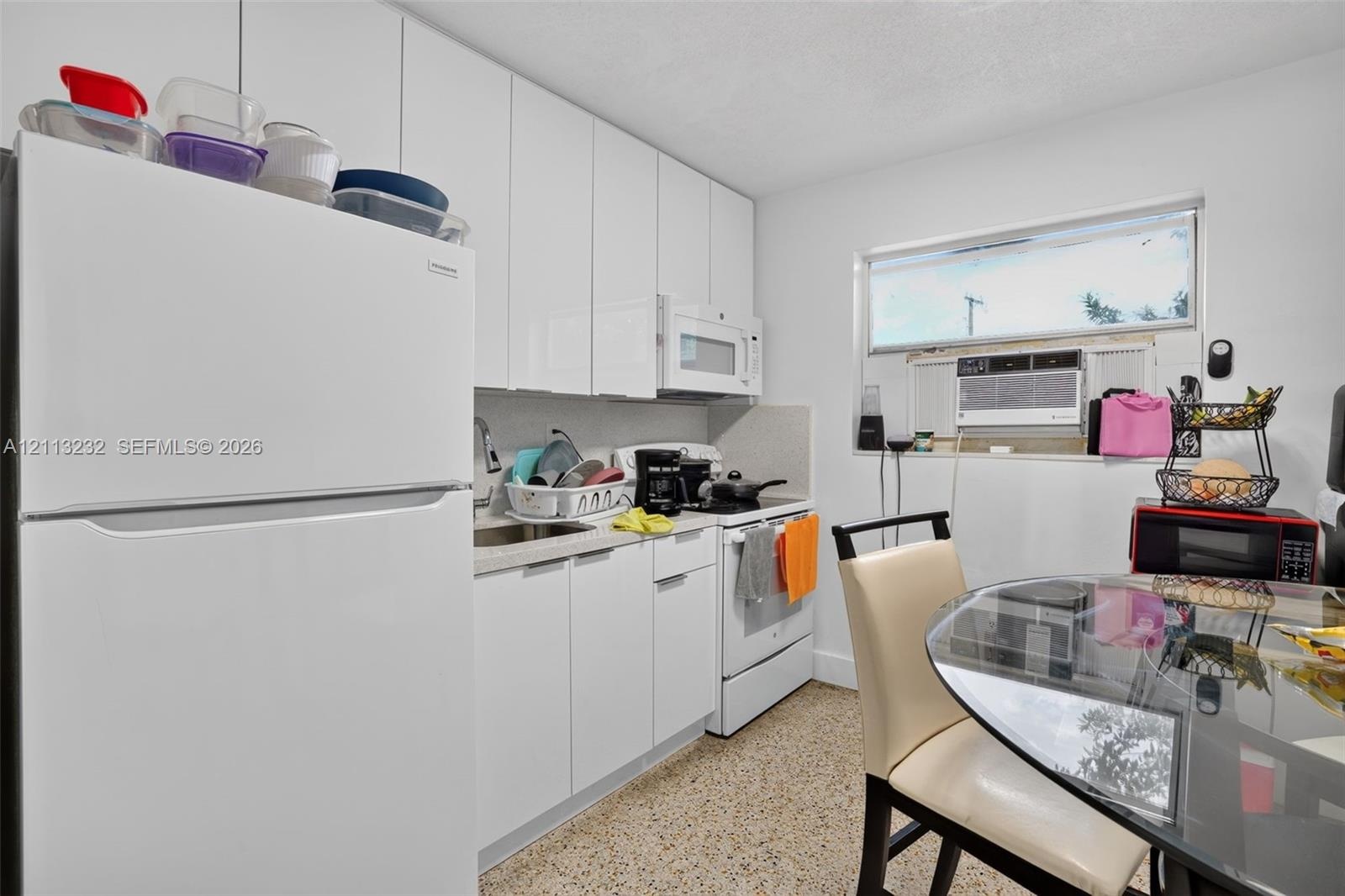 Kitchen featuring white flat-panel cabinetry, full-size white refrigerator, integrated microwave, and textured stone-finish flooring